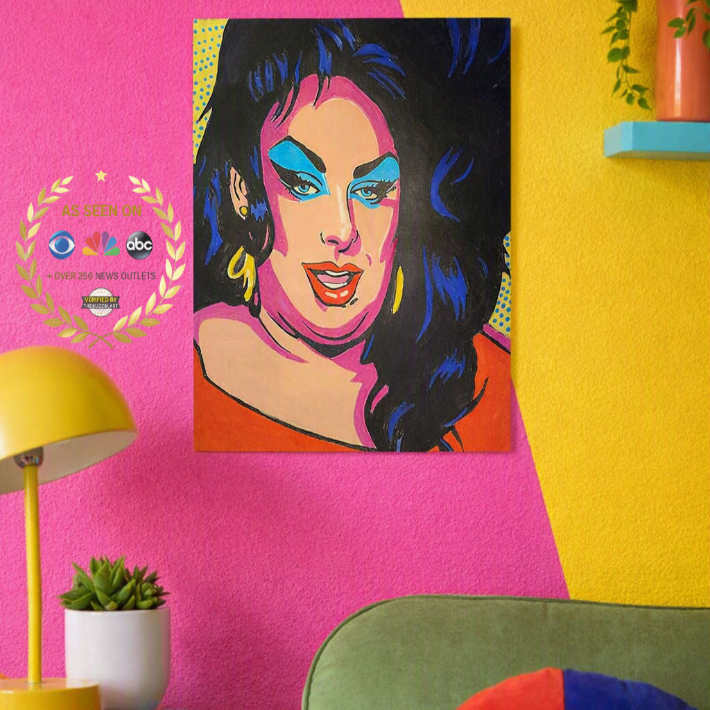 A colorful pop-art style portrait print of a woman with bold blue, pink, black, and orange tones, displayed on a bright pink wall in a styled room with a yellow lamp, small plant, and green chair.