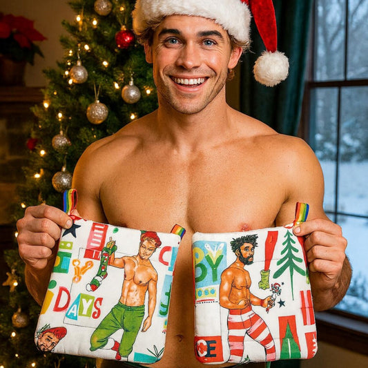 Sexy Man holding pot holders with Christmas-themed designs in front of a decorated Christmas tree.